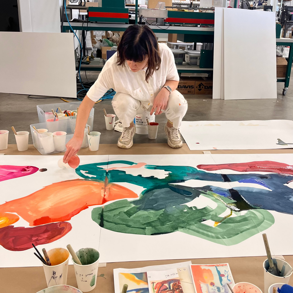 Person painting a large abstract artwork on a floor with various art supplies around.
