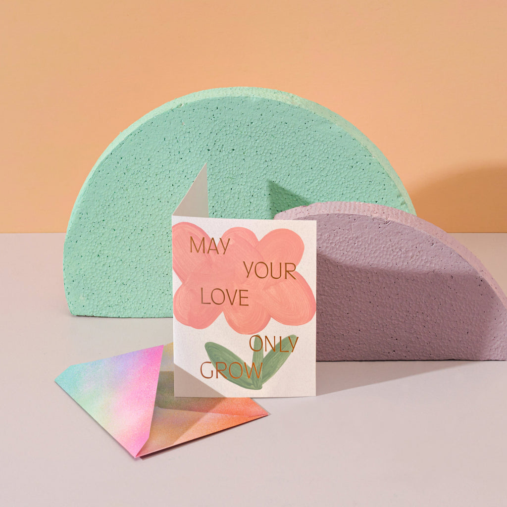 Two colorful shapes, with a card in front. The card has a hand-painted flower on it. 