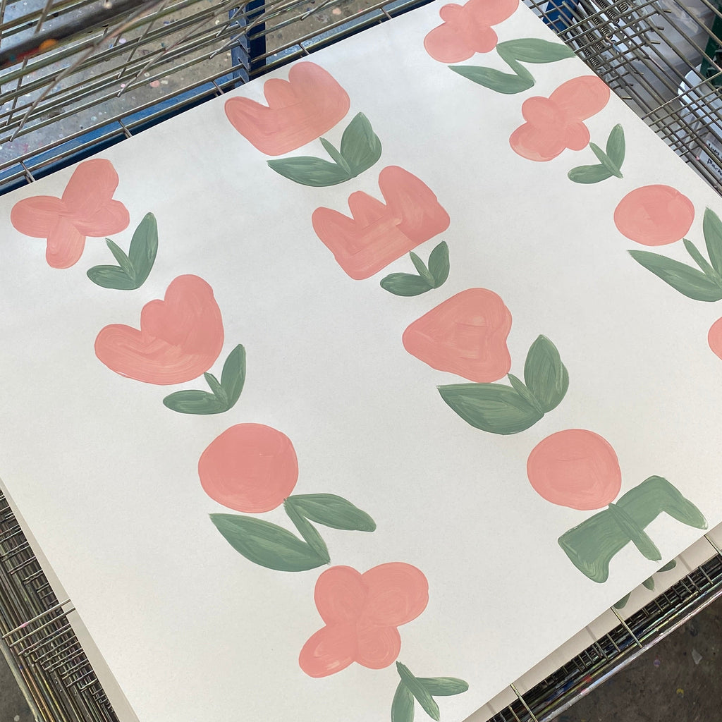 Paper with hand-painted pink flowers pattern on a white paper, placed on a metal drying rack.