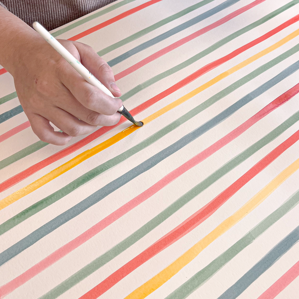Person painting a striped surface with a container of paint.